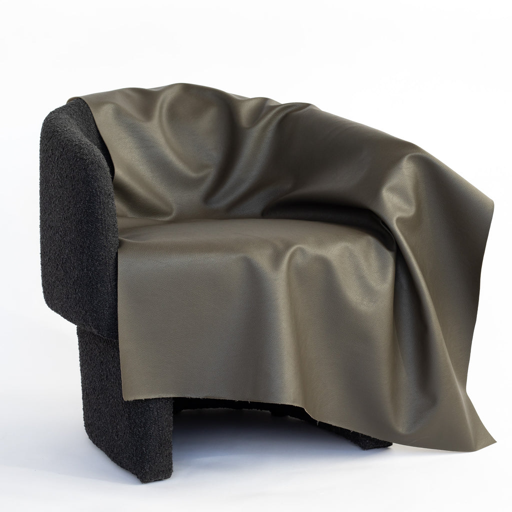 a charcoal grey with a subtle moss undertone performance vinyl faux leather upholstery fabric draped on a chair