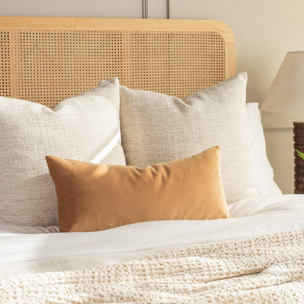 Camel toned velvet lumbar pillow on a queen bed with neutral textured throw pillows